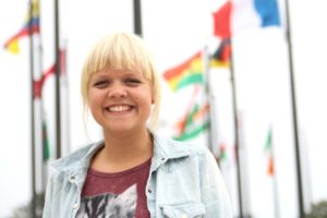 Miriam Grith Steiner på YWAMs hovedbase i Kona, Hawaii. I baggrunden ses flagene fra alle verdens nationer. De symboliserer den store bases mange nationaliteter samtidig med, at de er en påmindelse om Jesu missionsbefaling om at nå ud med evangeliet til alle verdens mennesker.