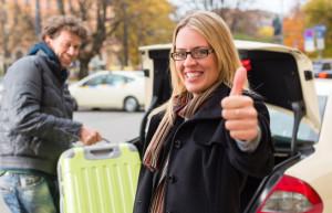 Young woman standing in front of taxi, she has reached her destination, the taxi driver will help with the luggage